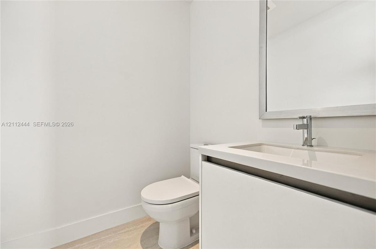 Modern vanity featuring a seamless integrated countertop and sink, wall-mounted mirror with a metallic frame, chrome faucet, and light-toned wood-fini