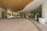 Covered porte-cochère featuring a curved wood-panel ceiling, herringbone-pattern paver drive, vertical slat wall detailing, and expansive glass entry 