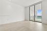 Large-format tile flooring, recessed ceiling lighting, and floor-to-ceiling sliding glass doors opening to a covered balcony with built-in cabinetry
