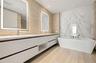 Dual-sink vanity with white cabinetry and countertop, backlit rectangular mirrors, freestanding soaking tub, and large-format tile surround