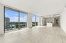Floor-to-ceiling glass windows, expansive stone-finish flooring, recessed lighting, integrated kitchen appliances, and a minimalist stone-top island