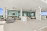 Covered terrace featuring large-format stone tile flooring, built-in stone bar counter, floor-to-ceiling glass paneling, and ceiling-mounted fans