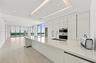 Modern kitchen featuring seamless flat-panel cabinetry, a spacious solid-surface island, built-in stainless steel appliances, recessed tray ceiling li
