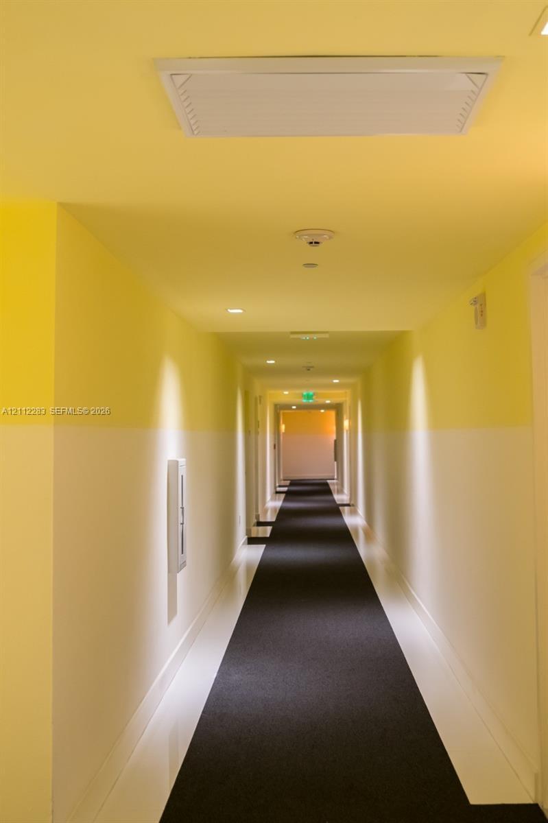 Hallway featuring two-tone wall paint, recessed ceiling lighting, a flush-mount overhead HVAC unit, integrated fire safety components, and dark wall-t