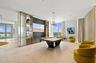Open-concept space featuring large-format tile flooring, floor-to-ceiling windows, a custom stone-clad media wall with built-in shelving, and recessed