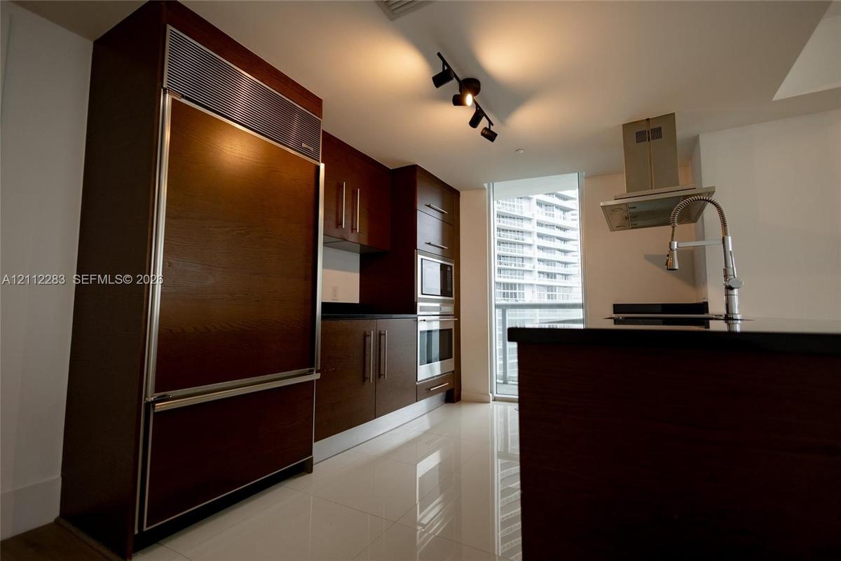 Kitchen featuring dark wood-finish cabinetry, stainless steel built-in appliances, a center island with a stone countertop, a gooseneck faucet, and hi