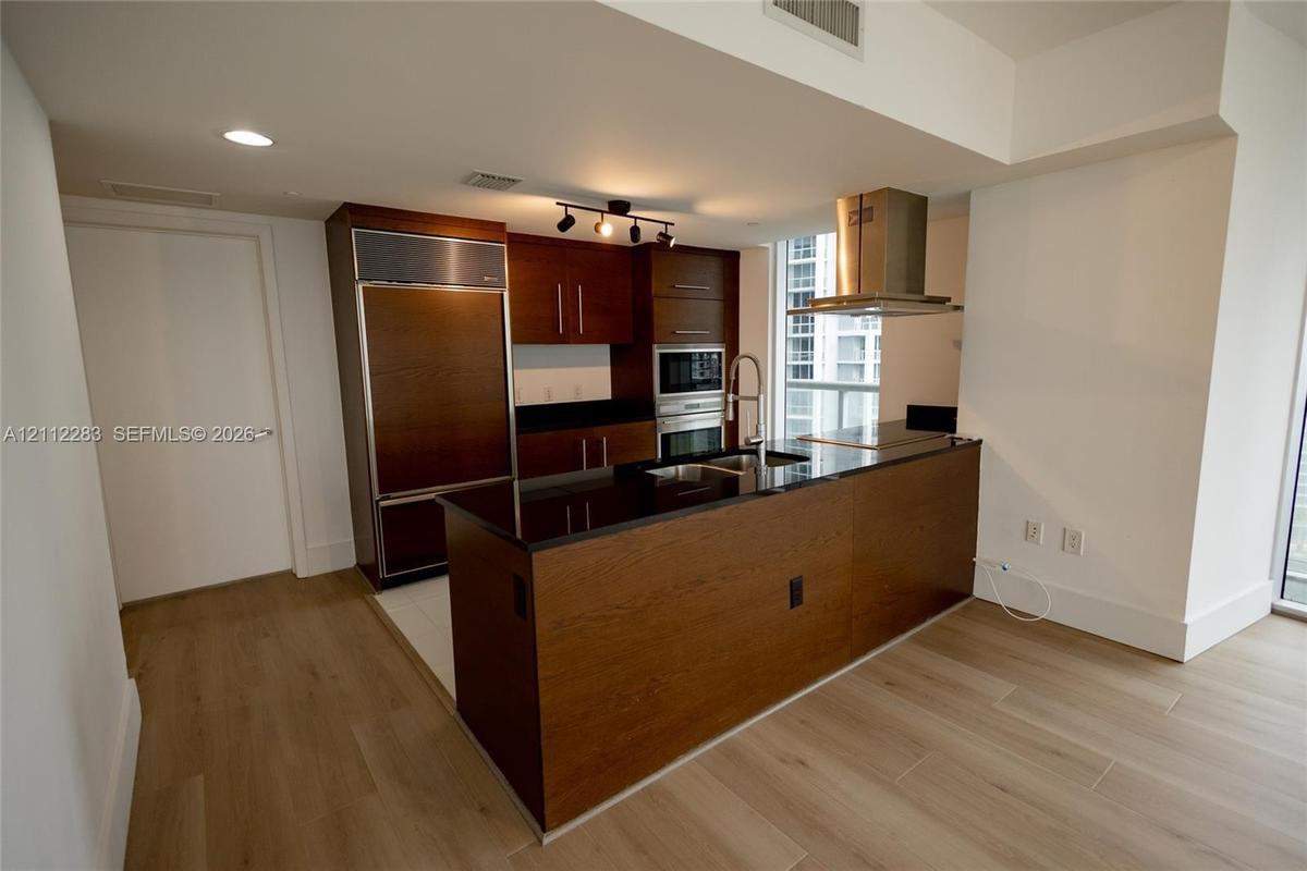 Kitchen featuring wood-finish cabinetry, dark stone countertops, stainless steel appliances including a built-in refrigerator and wall oven, and a cen