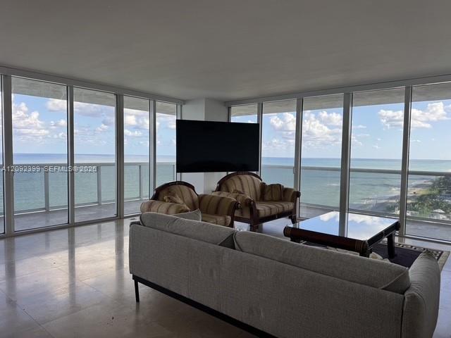 Floor-to-ceiling windows, polished tile flooring, and integrated glass-panel balcony railings featuring an expanse of ocean scenery