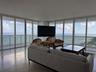 Floor-to-ceiling windows, polished tile flooring, and integrated glass-panel balcony railings featuring an expanse of ocean scenery