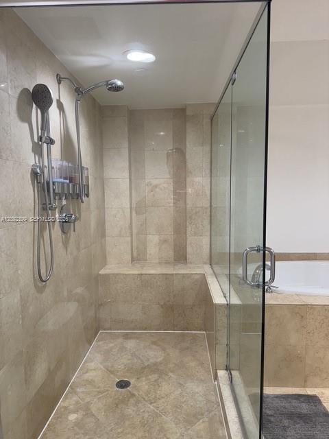 Walk-in shower featuring floor-to-ceiling neutral tile, built-in tiled bench, frameless glass enclosure, and dual-head rainfall and handheld shower fi