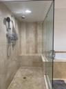 Walk-in shower featuring floor-to-ceiling neutral tile, built-in tiled bench, frameless glass enclosure, and dual-head rainfall and handheld shower fi