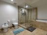 Frameless glass shower enclosure with stone wall tile, separate soaking tub with stone surround, bidet, and neutral floor tile