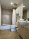 Bathroom featuring a tub-shower combination with tile surround, a wall-mounted storage cabinet, a vanity with a drop-in sink, and stone-finish floorin