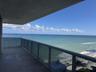 Covered balcony featuring concrete flooring and a structural glass-paneled railing with a metal handrail, overlooking the ocean
