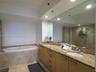 Dual-sink vanity with stone countertop and flat-panel cabinetry, recessed lighting, expansive wall-to-wall mirror, built-in soaking tub with stone sur