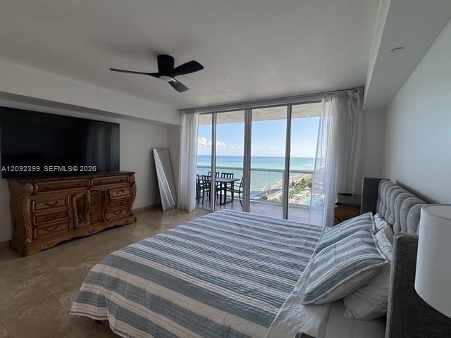 Floor-to-ceiling glass sliders, stone tile flooring, ceiling fan, and private balcony overlooking the ocean