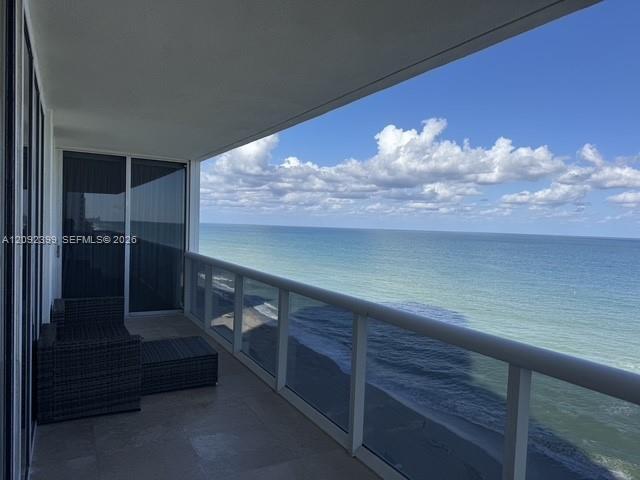 Covered balcony featuring stone tile flooring and a glass railing, overlooking the ocean