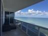 Covered balcony featuring stone tile flooring and a glass railing, overlooking the ocean