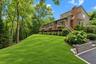 Exterior featuring vertical wood-finish siding, a red brick chimney, an elevated wood deck, stone-block retaining walls, and a manicured lawn