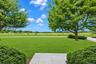 Expansive lawn featuring mature trees, manicured hedges, a paved walkway, and wire fencing