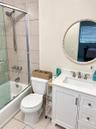 White vanity featuring a solid surface countertop, rectangular undermount sink, and brushed-finish fixtures, paired with a glass-enclosed shower with 