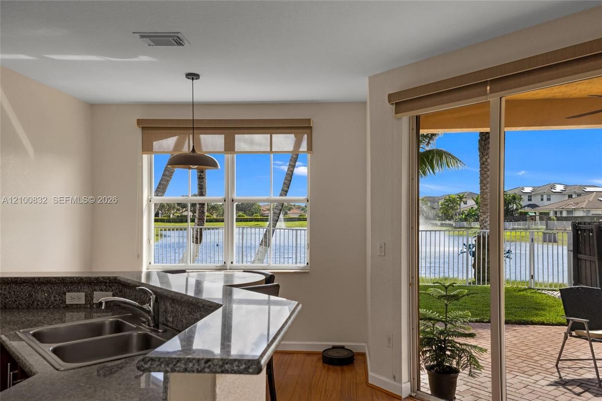 Kitchen featuring a stone-surfaced breakfast bar, double-basin stainless steel sink, wood-finish flooring, and sliding glass doors opening to a brick-