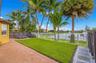 Fenced backyard featuring a brick-paver patio, manicured lawn, mature palm trees, and waterfront perimeter