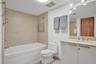 Bathroom featuring a deep soaking tub with neutral tile surround, vanity with stone-finish countertop, undermount sink, and full-width vanity mirror w