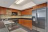 Kitchen featuring wood cabinetry, dark stone-finish countertops, multi-toned glass tile backsplash, recessed tray ceiling, and stainless steel applian