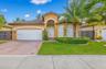 Stucco exterior featuring a tiled roof, arched entryway, paved driveway, and manicured landscaping