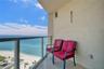 Covered balcony with stone-tile flooring and glass panel railing overlooking the oceanfront