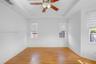 Room featuring a tray ceiling, wood-finish flooring, three windows with fitted horizontal blinds, and a central ceiling fan with integrated lighting