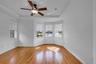 Tray ceiling with a central multi-blade ceiling fan, wood-finish flooring, and a bay window configuration featuring horizontal shade treatments
