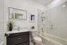 Bathroom featuring a dark wood-finish vanity with a white countertop, rectangular sink, glass-enclosed shower-tub combination, and tiled walls
