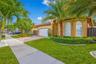 Stucco exterior featuring an arched entryway, paver driveway, two-car garage, and arched windows accented by landscaped shrubbery and palm trees