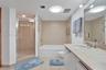 Bathroom featuring a glass-enclosed shower, deep soaking tub, tile surround, stone-composite vanity countertop, and wall-mounted mirror