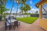 Outdoor space featuring brick paver patio, manicured lawn, white aluminum perimeter fencing, and mature palm trees