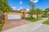 Stucco exterior with an arched entryway, tile roof, multi-car garage, and herringbone-patterned paved driveway, surrounded by mature palm trees and ma