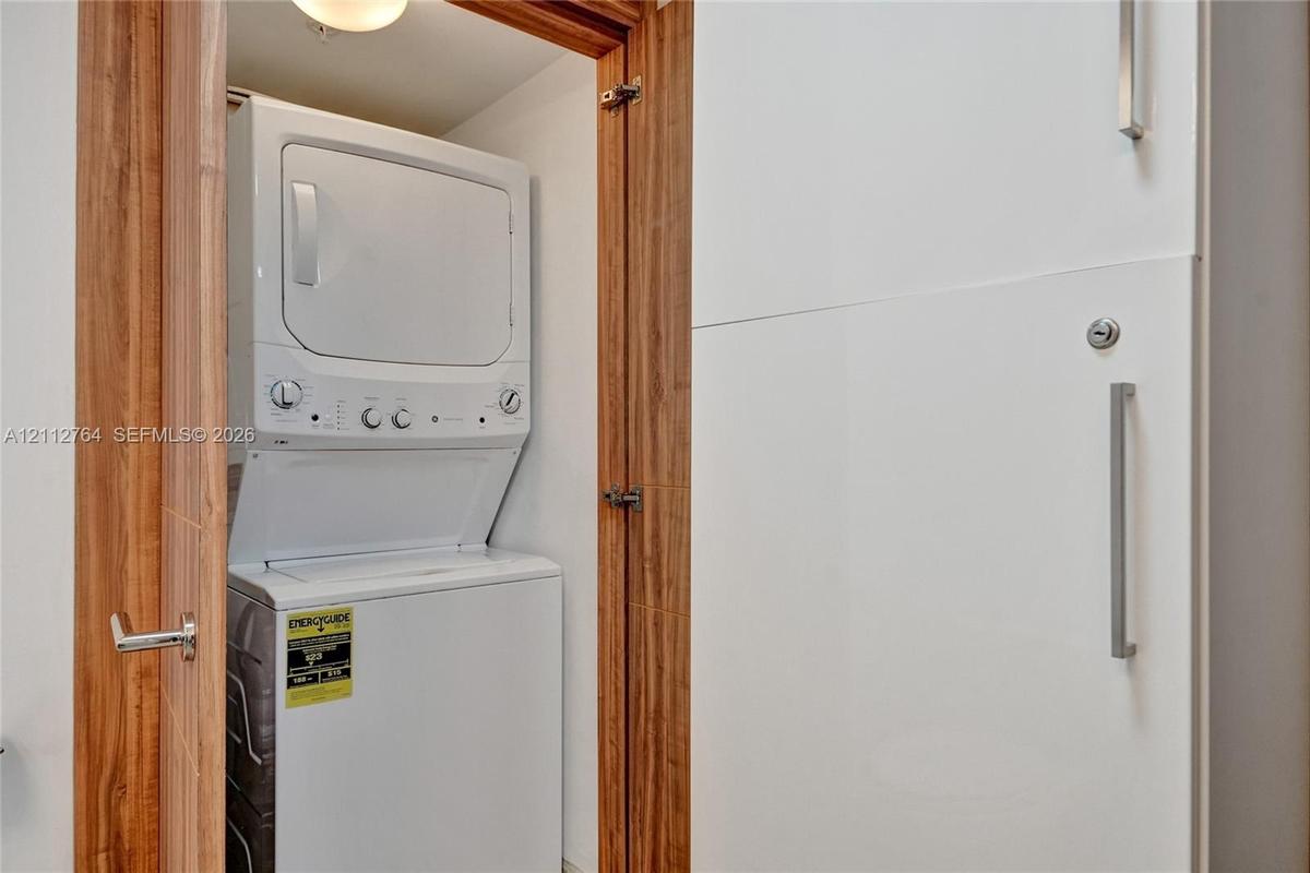 Stacked laundry appliance set within a recessed closet featuring wood-finish door frames and integrated cabinetry with brushed metal hardware