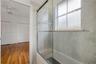 Bathroom featuring a glass-enclosed tub with metal hardware, light-toned wall tile, and a privacy-glass window