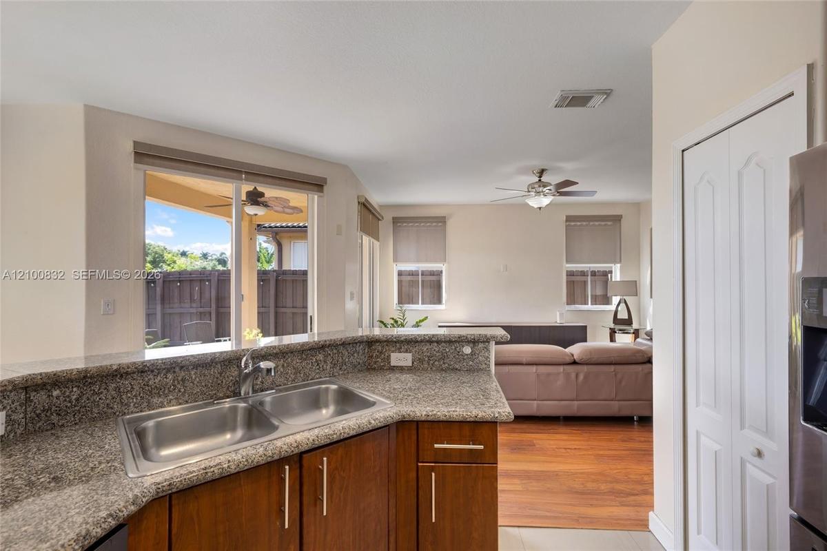 Kitchen featuring a raised breakfast bar with stone-finish countertops, stainless steel dual-basin undermount sink, and wood-finish cabinetry