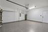 Garage featuring large-format tile flooring, white finished walls, wall-mounted climate control unit, water heater, and interior access door