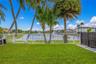 Lawn area featuring white metal perimeter fencing, mature palm trees, and a decorative water feature