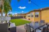 Rear yard featuring a paved herringbone brick patio, manicured lawn, perimeter wood fencing, and a covered lanai