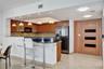 Kitchen featuring wood-finish cabinetry, stone countertop breakfast bar, mosaic tile backsplash, pendant lighting, and full-height wood-finish door wi