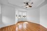 Tray ceiling featuring a central five-blade ceiling fan with integrated lighting, wood-finish flooring, and bay windows with horizontal blinds