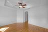 Tray ceiling with a central multi-blade ceiling fan, wood-finish flooring, and a decorative arched doorway