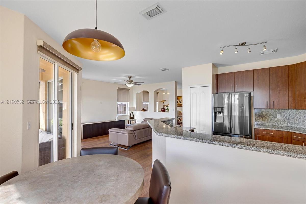 Kitchen featuring stone countertops, dark wood cabinetry, stainless steel refrigerator, dome pendant lighting, and wood-finish flooring