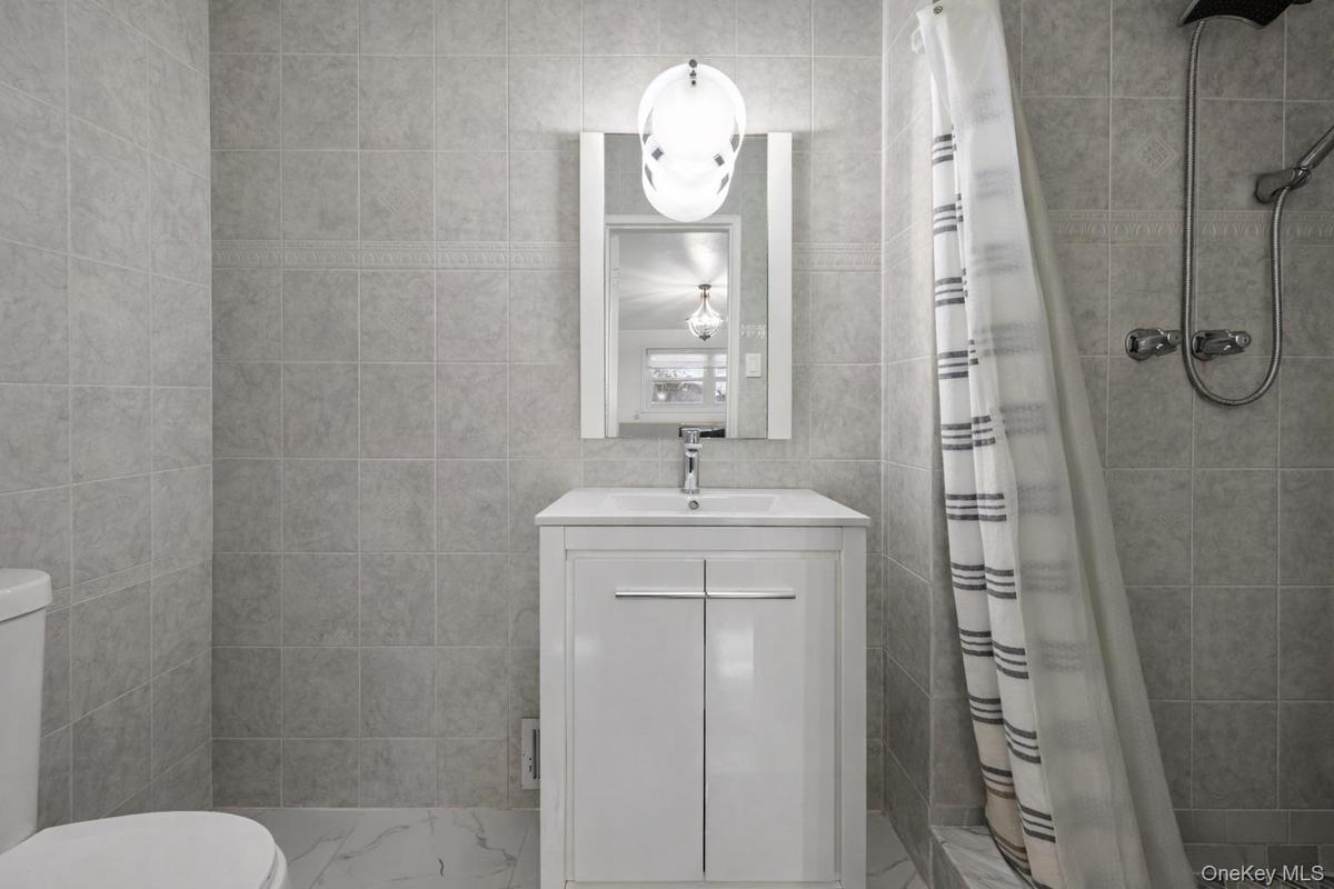 Bathroom featuring full-height neutral wall tiling, vanity with a white integrated sink, polished chrome faucet, wall-mounted globe lighting fixture, 