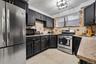 Kitchen featuring dark cabinetry with gold-tone hardware, stainless steel appliances, stone-surface countertops, stone tile backsplash, and tile floor